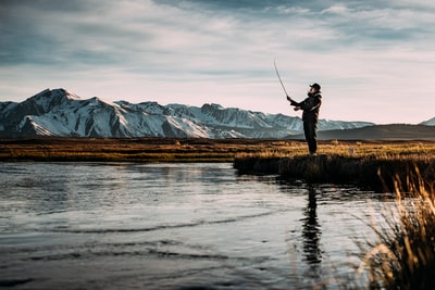 在阿尔卑斯山附近的河流上钓鱼的人的风景照片